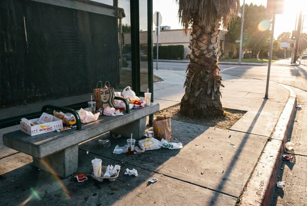 Littered bus stop corner with scattered wrappers and cups