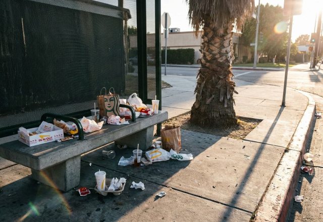Littered bus stop corner with scattered wrappers and cups